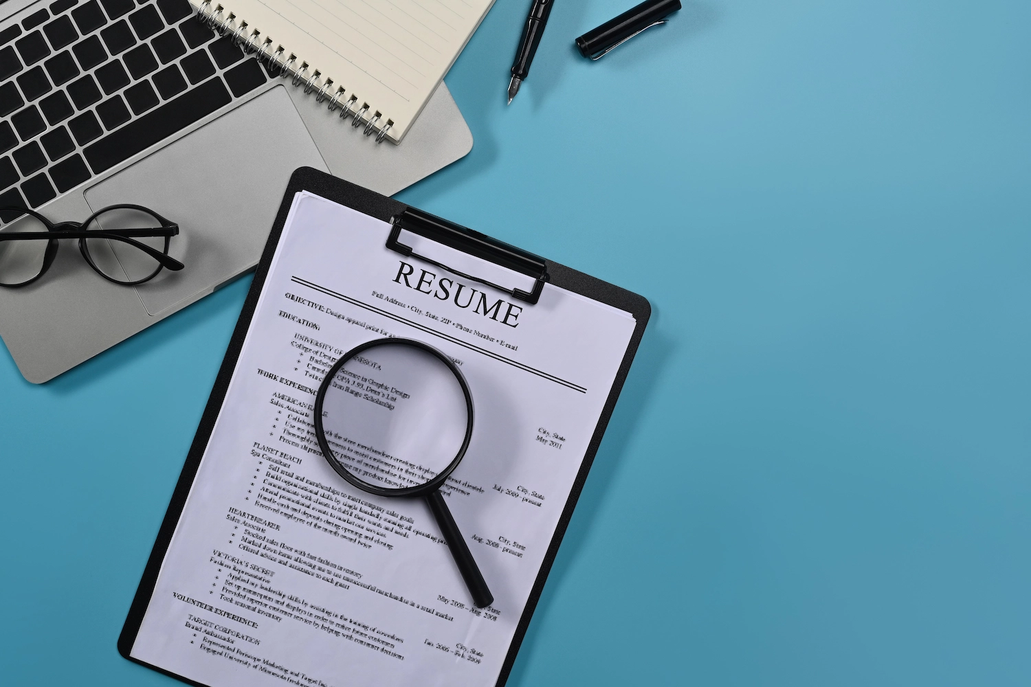 top view of laptop and resume document with a magnifying glass